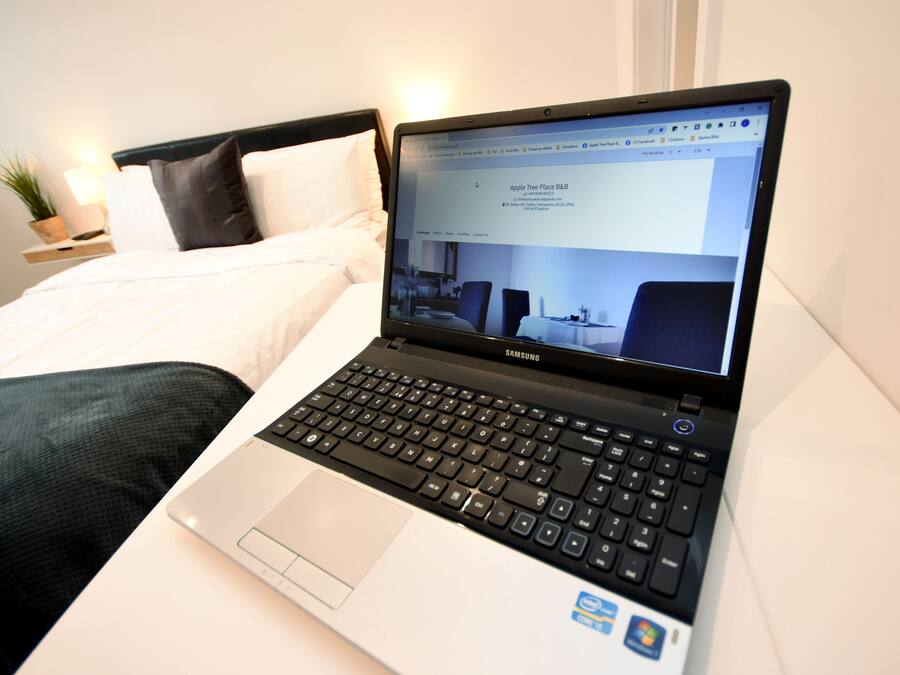 Una laptop sobre una cama con una colcha blanca y almohadas negras.