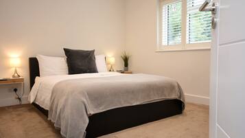 A bedroom with a bed, bedside lamps, a window with blinds, and a door.