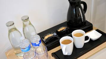 A tray with a black coffee maker, two white mugs, two clear glasses, and two water bottles on a wooden surface.