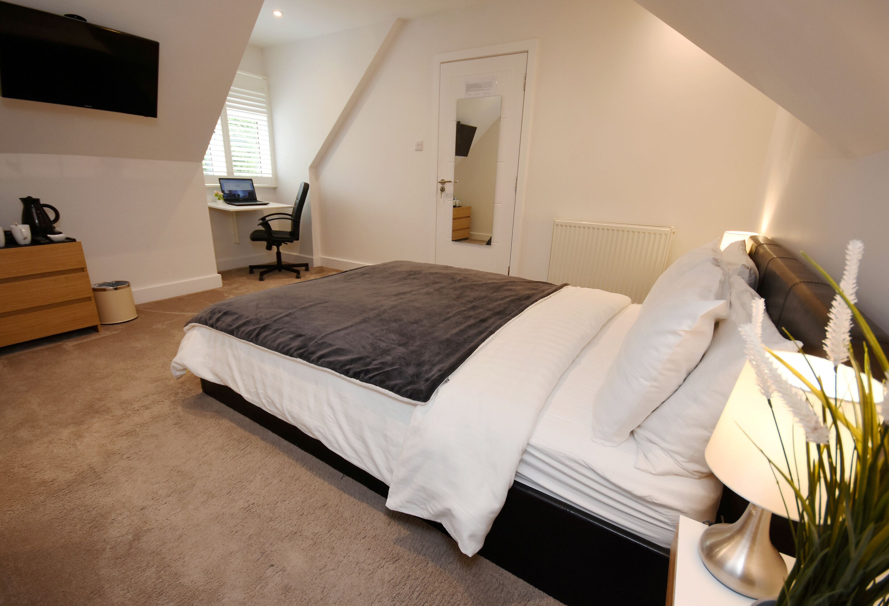 A bedroom with a bed, a desk, a chair, a dresser, and a TV.