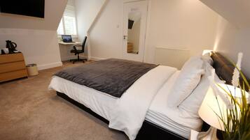 A bedroom with a bed, a desk, a chair, a dresser, and a TV.