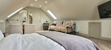 Quarto com cama, penteadeira, cômoda, sofá, televisão e claraboia.