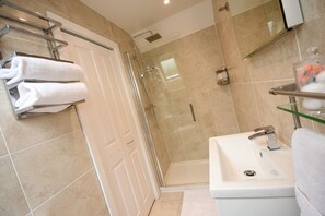 A modern bathroom with a glass shower enclosure, a white sink, and a towel rack with folded towels. - Apple Tree Place B&B (Tadley)