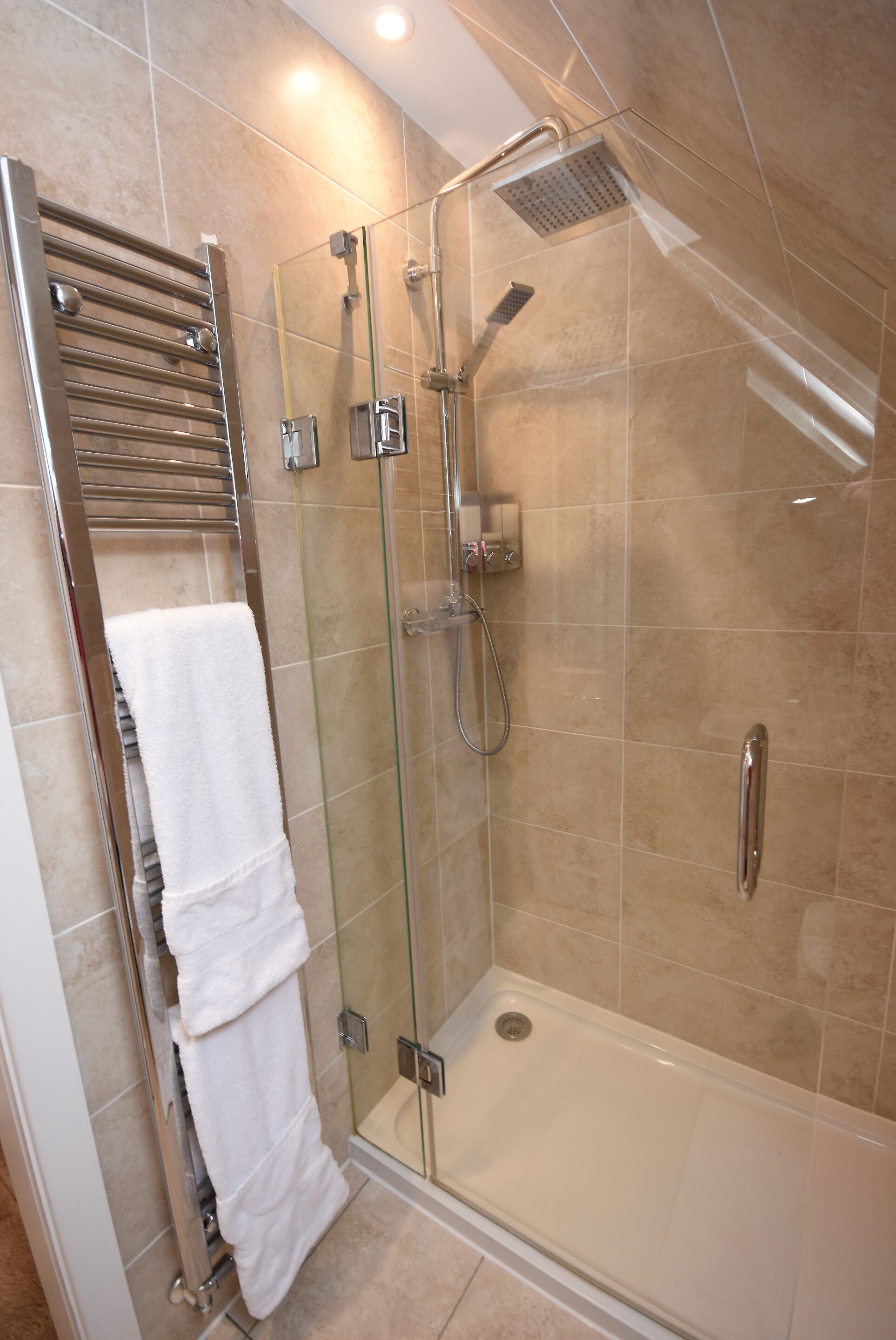 Una ducha con cerramiento de vidrio, cabezal de ducha manual y panel de control en la pared.