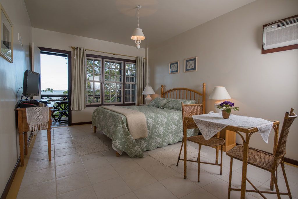 Un dormitorio con cama, dos mesitas de noche con lámparas, televisor, mesa de comedor con sillas y ventana con cortinas.