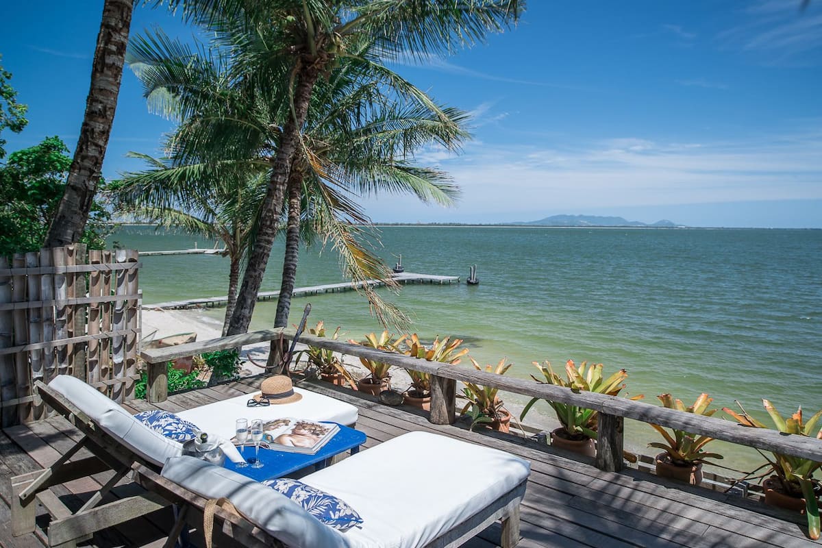 A wooden deck with lounge chairs and a table, overlooking a calm sea with a distant shoreline.