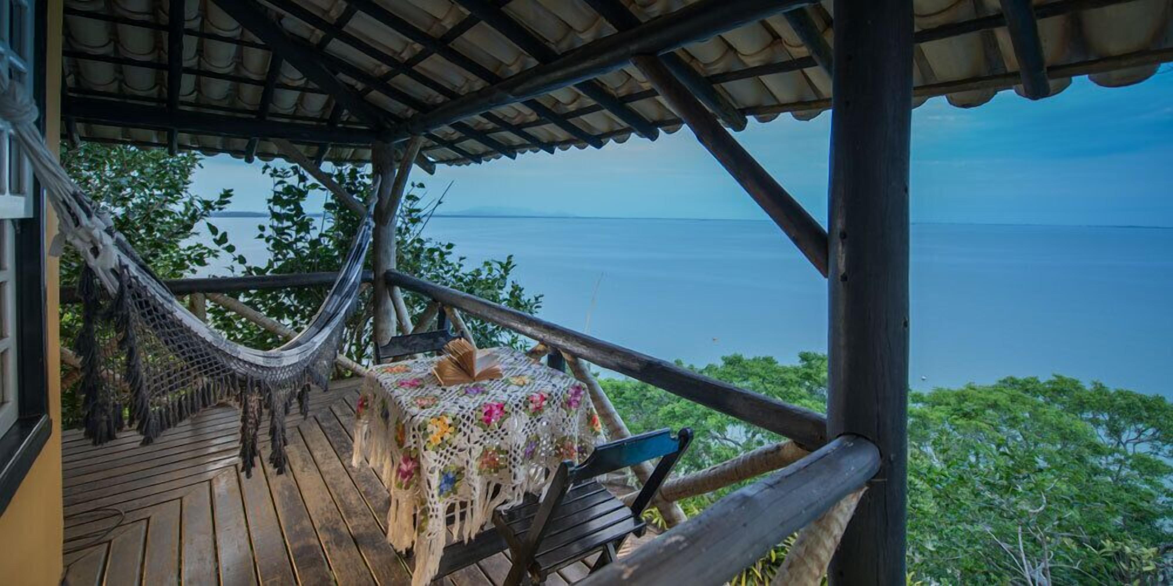 Une terrasse en bois avec un hamac, une table recouverte d’une nappe à motifs floraux et un banc.