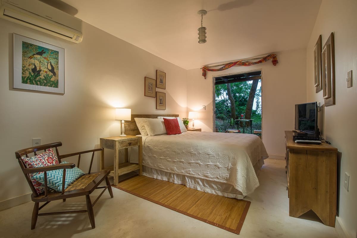 A bedroom with a bed, bedside tables, a chair, a television, and a window with a view of trees.