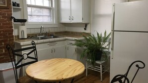Una cocina con armarios blancos, un lavamanos, un refrigerador, una mesa de madera y sillas.