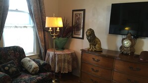 Una sala de estar con un sofá floral, un mueble de madera, una lámpara de pie verde, una estatua de león, un reloj y un televisor.