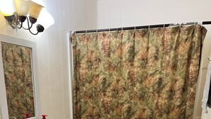 Et badeværelse med en hvid vask, toilet og badeforhæng. Der er et spejl over vasken, og et håndklædetørrestativ er synligt.