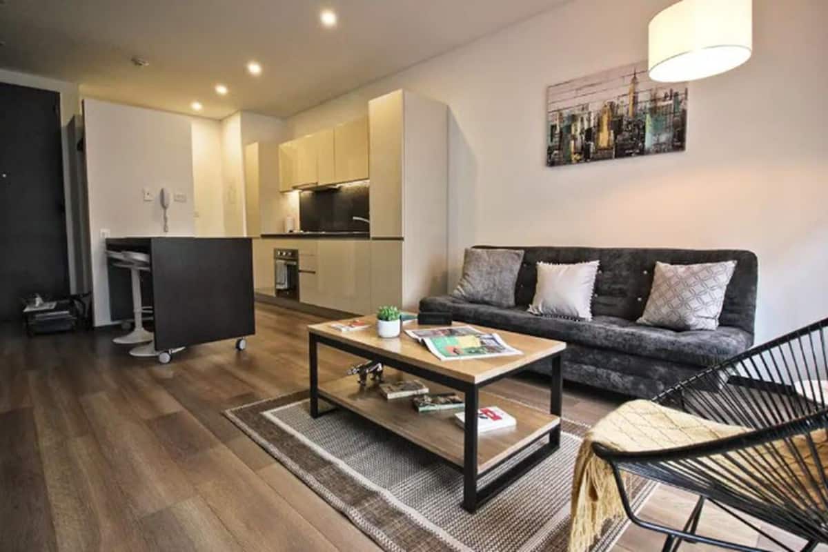 Uma sala de estar moderna com sofá, mesa de centro e área de refeições, com cozinha ao fundo.