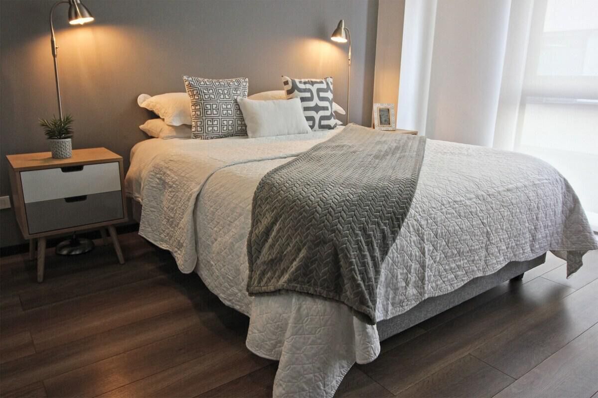 Un dormitorio con cama, lámparas de noche, mesita de noche y una pequeña planta en maceta.