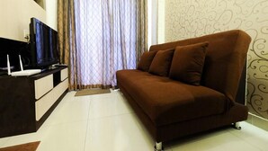 Ein Wohnzimmer mit braunem Sofa, einem Fernseher auf einem Schrank und einer Wand mit Muster.