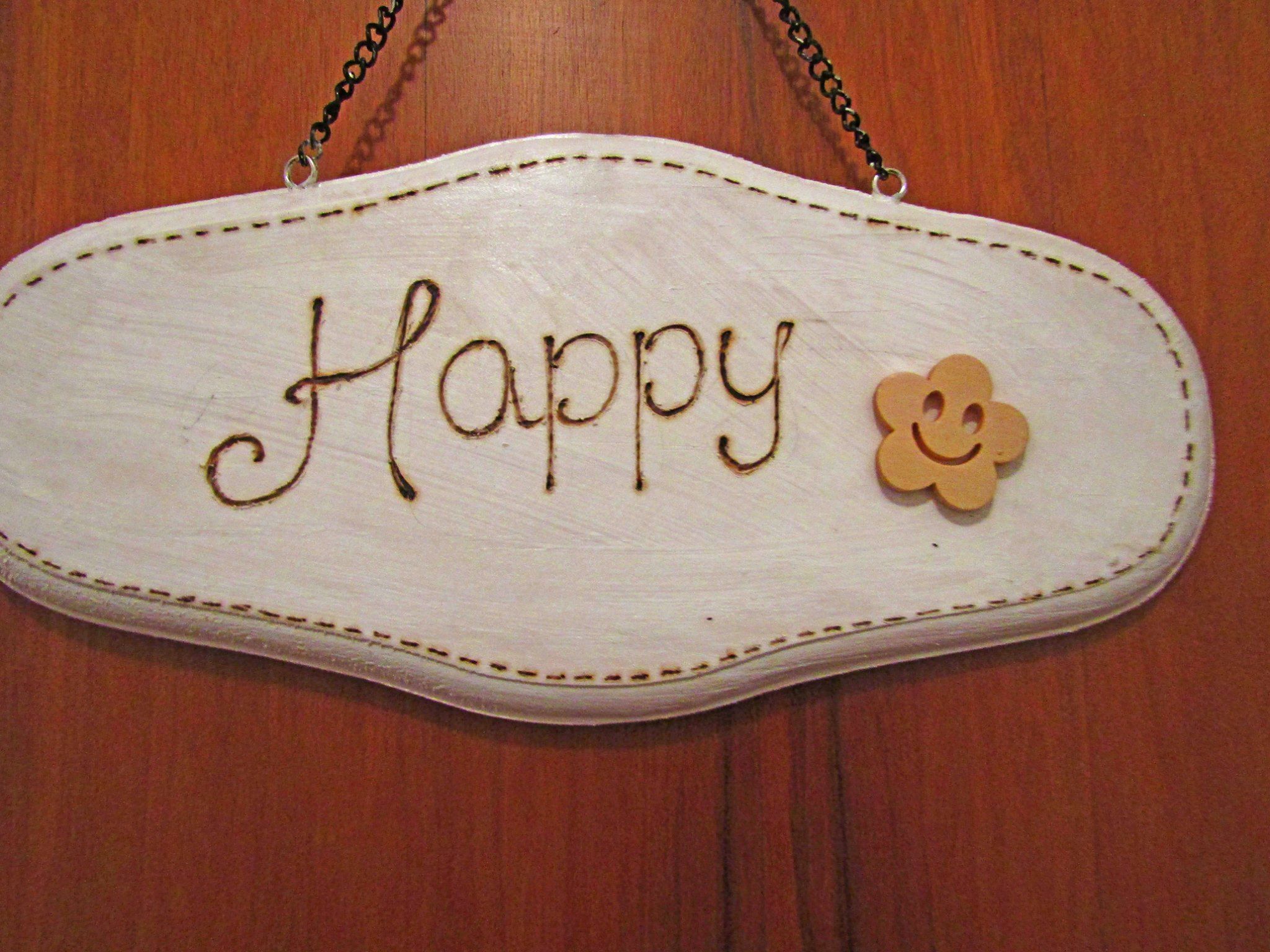 Een wit, ovaal bordje met de tekst 'Happy' en bloemdecoratie.