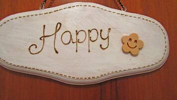 Een wit, ovaal bordje met de tekst 'Happy' en bloemdecoratie.