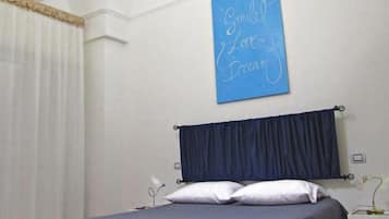 A bedroom with a bed, a blue wall sign, a window with white curtains, and a ceiling light.