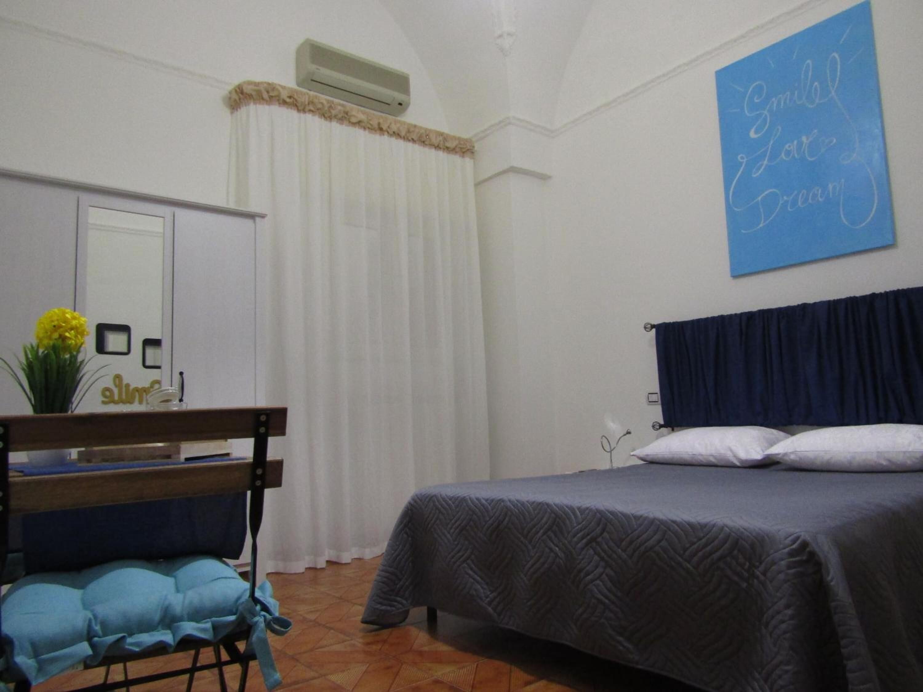Un dormitorio con cama, escritorio, silla, espejo y una pared con una cita motivacional.