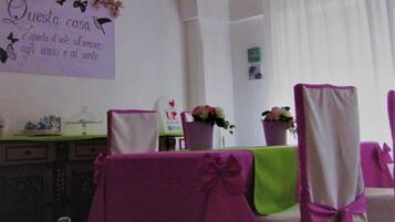 A dining area with a table set for four, chairs with purple sashes, a wall clock, and a sign with Italian text.