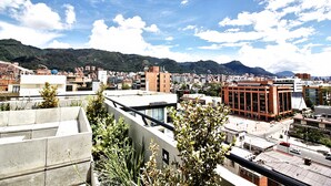 A cityscape with modern buildings, a prominent red building, and a mountainous backdrop under a partly cloudy sky. - Virrey Condos By Velvet Luxury (Bogotá)