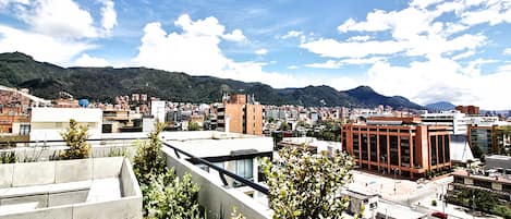 A cityscape with modern buildings, a prominent red building, and a mountainous backdrop under a partly cloudy sky.