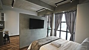 A modern bedroom with a large bed, a flat-screen TV mounted on the wall, and a window with curtains. - Virrey Condos By Velvet Luxury (Bogotá)