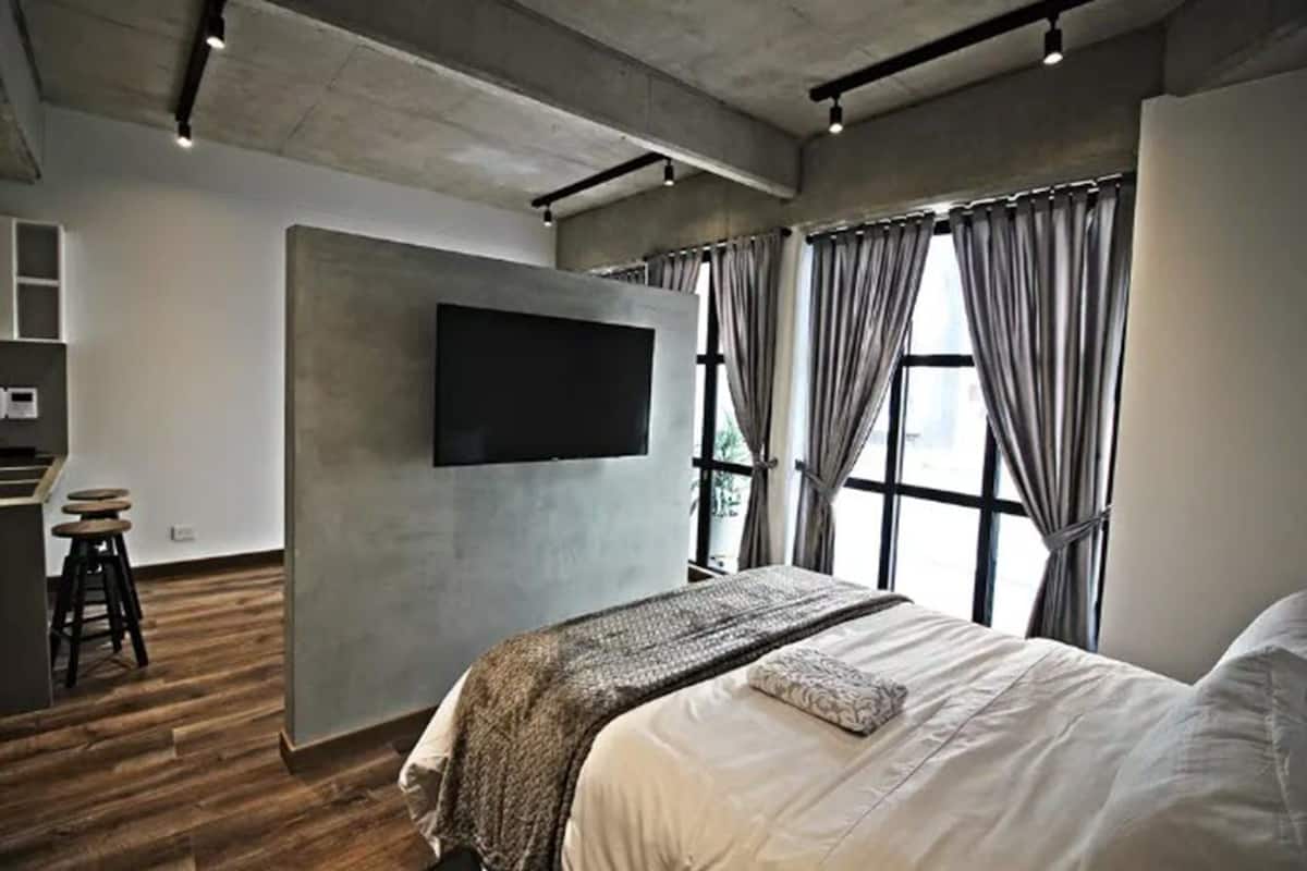Ein modernes Schlafzimmer mit einem großen Bett, einem flachbildfernseher an der Wand und einem Fenster mit Vorhängen.
