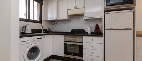 Cozinha compacta com máquina de lavar, forno, micro-ondas e frigorífico.
