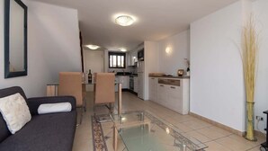 A modern living room with a glass coffee table, a sofa, and a dining area with chairs. - Parque Santiago I 242 - One Bed (Playa de la Américas)