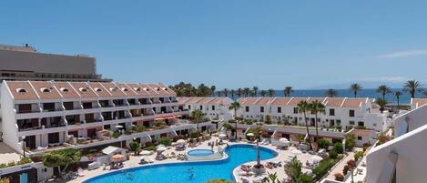 Un hôtel doté d’une grande piscine entourée de transats et de parasols, avec vue sur la mer.