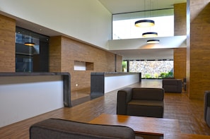 Um lobby moderno com piso de madeira, áreas de estar e uma parede de pedra com vista.