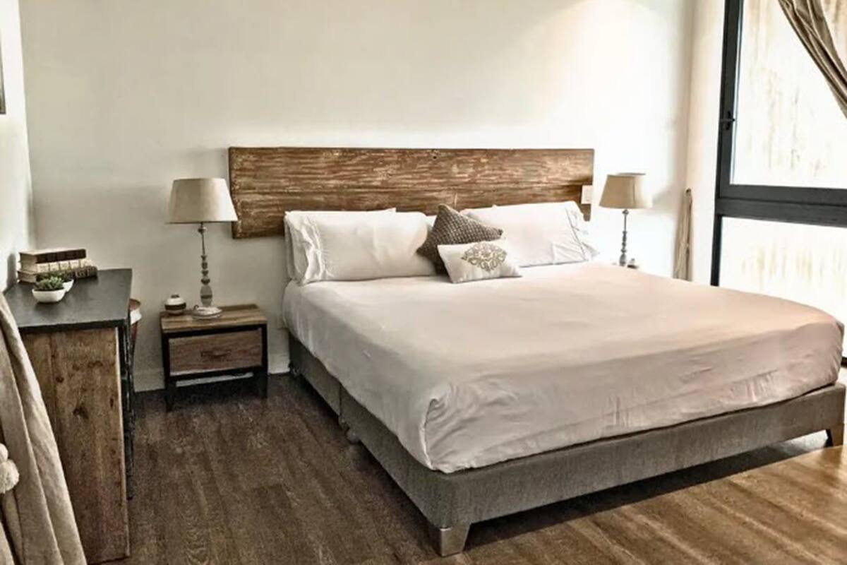 A neatly made bed with a wooden headboard, two bedside tables with lamps, and a view of the outdoors through a window.