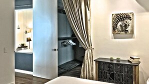 Une chambre d’hôtel moderne avec un grand lit, une petite console agrémentée d’objets décoratifs, une sculpture de Bouddha fixée au mur et une vue sur la salle de bain.