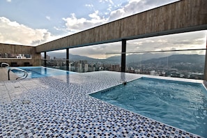 Piscina infinita no terraço com vista para a cidade, guarda-corpo de vidro e piso ladrilhado.