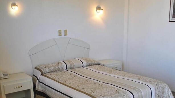 Una cama individual con cabecera, dos mesitas de noche y dos lámparas de pared.