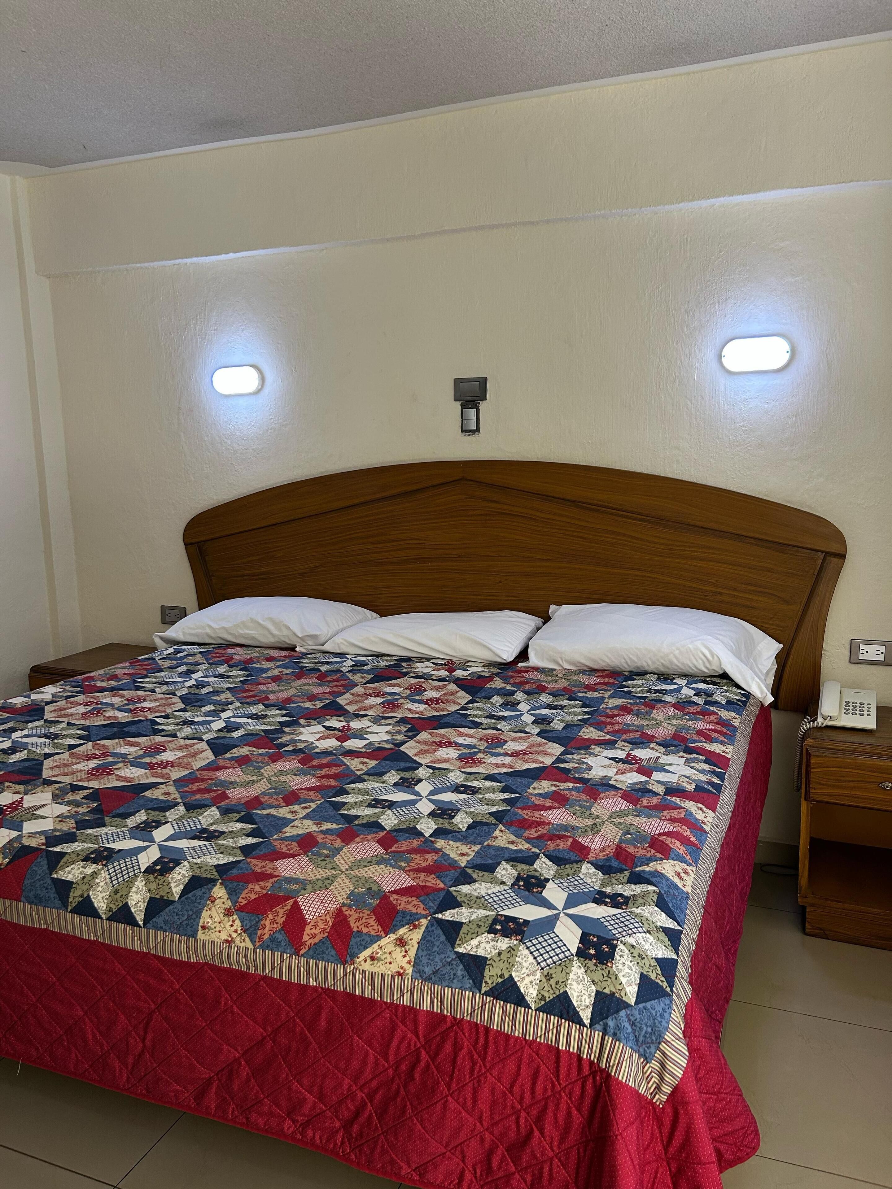 A bed with a patterned quilt, a wooden headboard, two bedside lamps, and a bedside telephone.