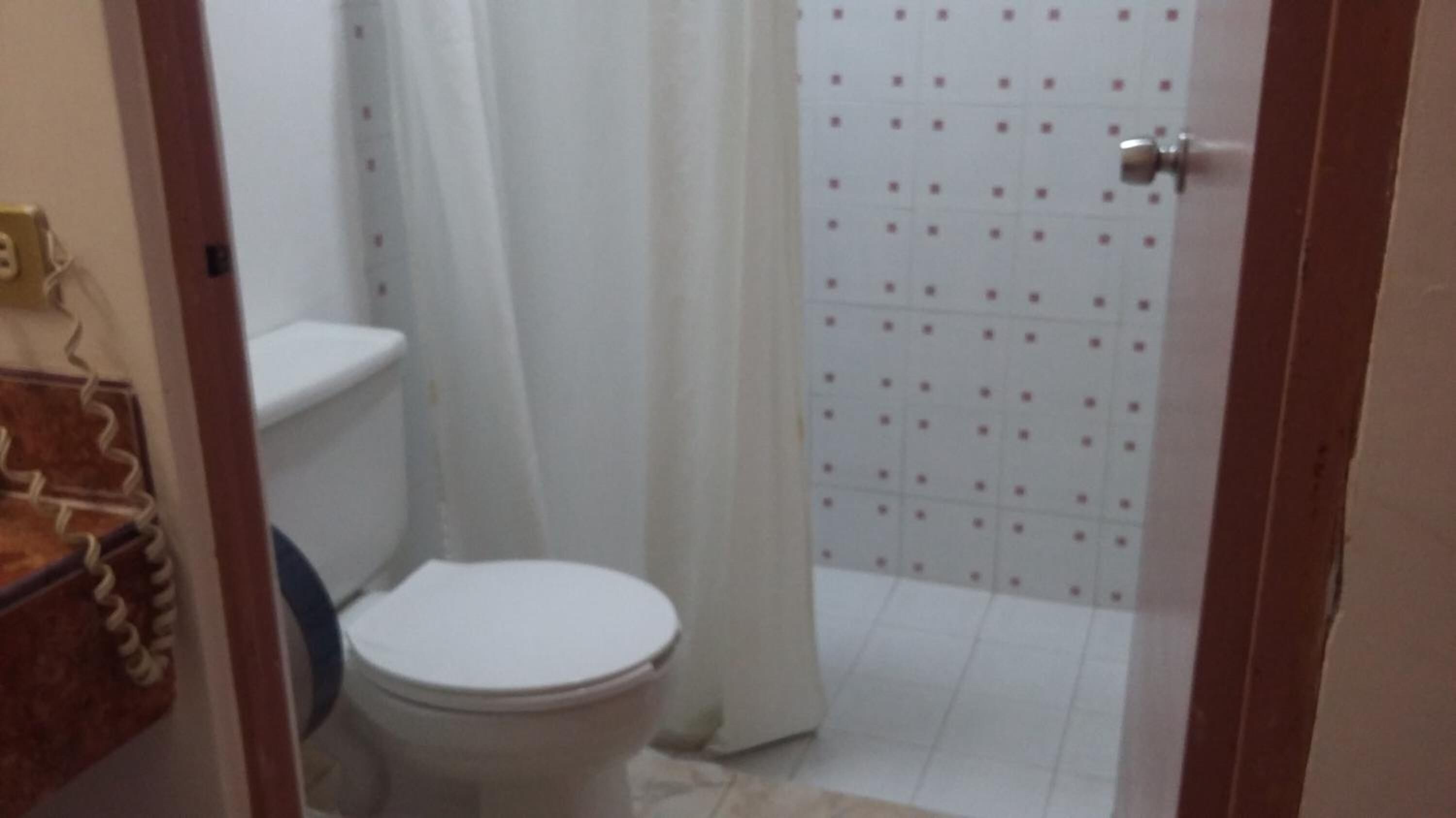 Un baño con inodoro, cortina de ducha y suelo de baldosas.