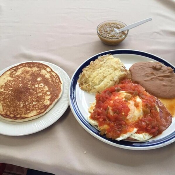 Um prato com panquecas, purê de batata, feijão e um prato à base de tomate.