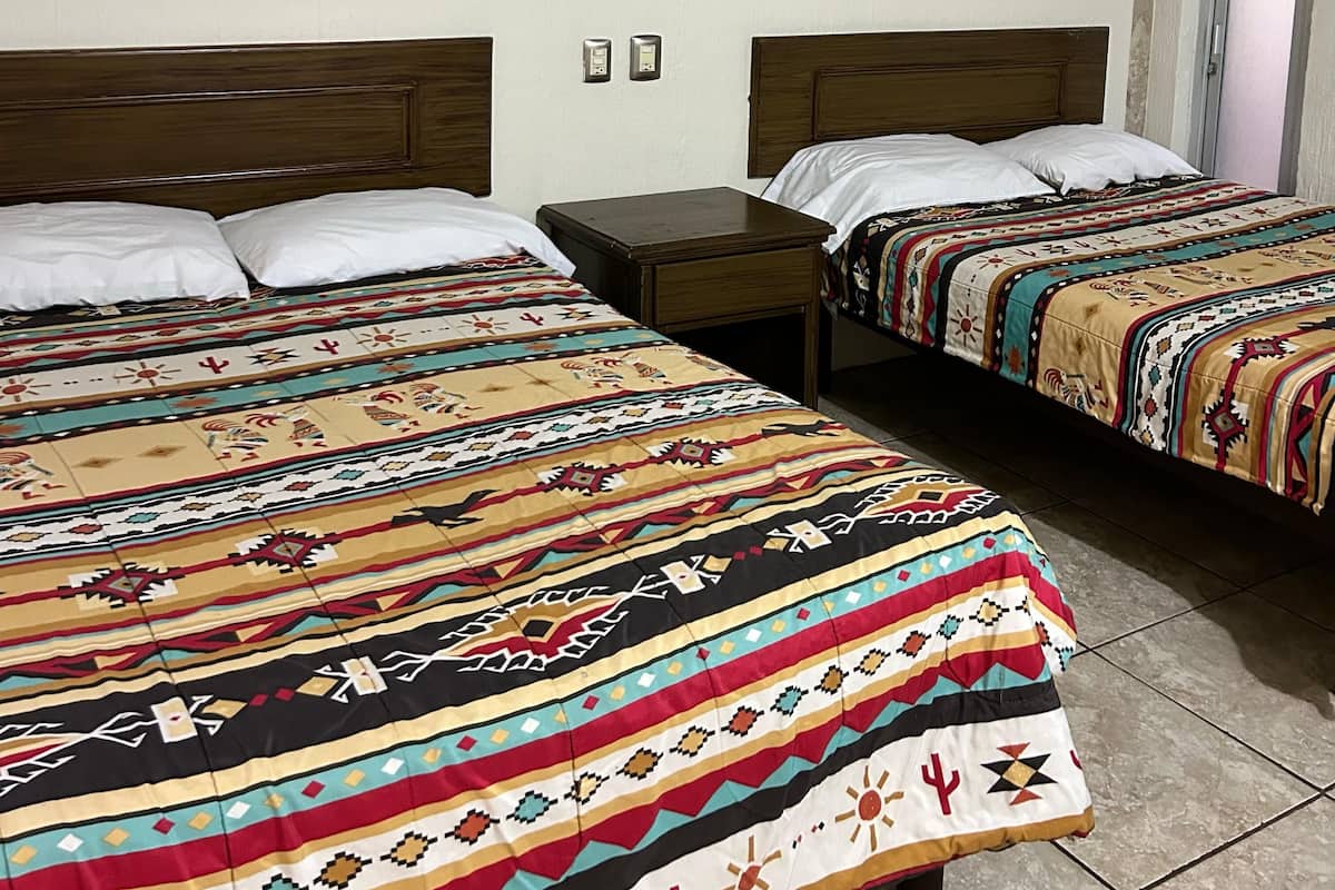 Une chambre d’hôtel avec deux lits, chacun agrémenté d’une couvre-lit à motifs, d’une tête de lit en bois et d’une table de chevet avec une lampe.