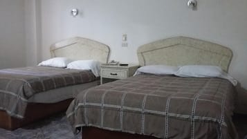 Dos camas individuales con cabeceras, una mesita de noche con cajón y un enchufe en la pared.