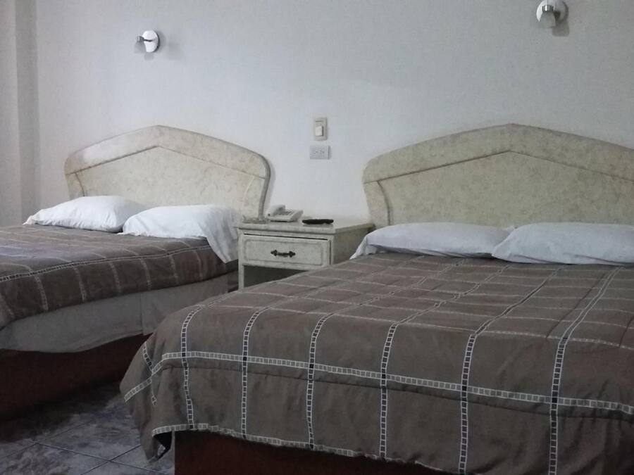 Dos camas individuales con cabeceras, una mesita de noche con cajón y un enchufe en la pared.
