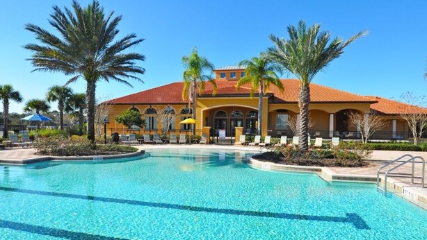 A hotel with a large pool, palm trees, and a red-tiled roof. - 6 Bed Pool Home w/ 2 Master Rooms at Watersong (Davenport)