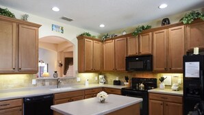 A kitchen with wooden cabinets, a black microwave, a dishwasher, and a refrigerator. - 6 Bed Pool Home w/ 2 Master Rooms at Watersong (Davenport)