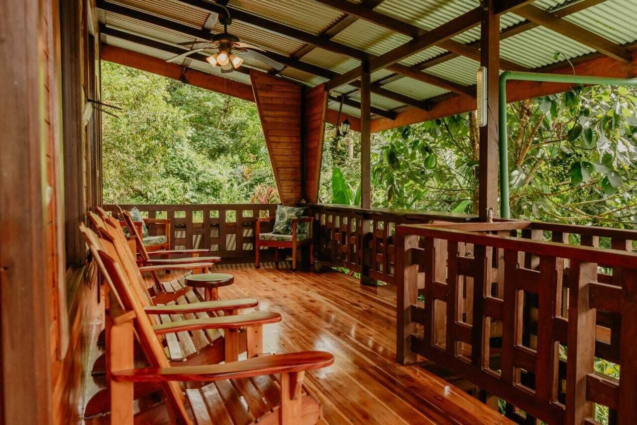 Un'area relax all'aperto con sedute e tavoli in legno, circondata da una recinzione di legno e con vista su una rigogliosa foresta verde.