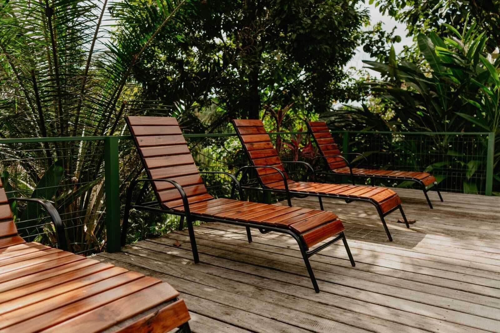 Outdoor wooden lounge chairs on a wooden deck surrounded by greenery.