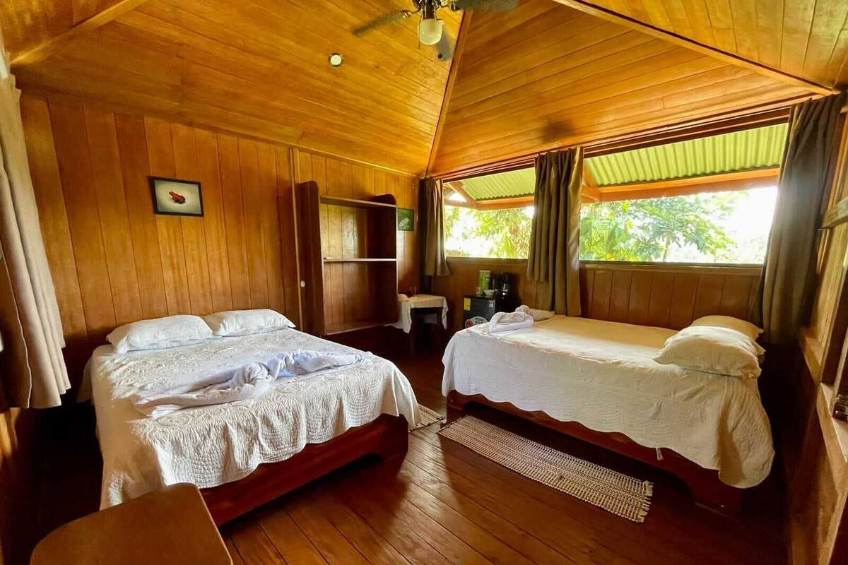 A wooden cabin with two beds, a small table, and a chair.
