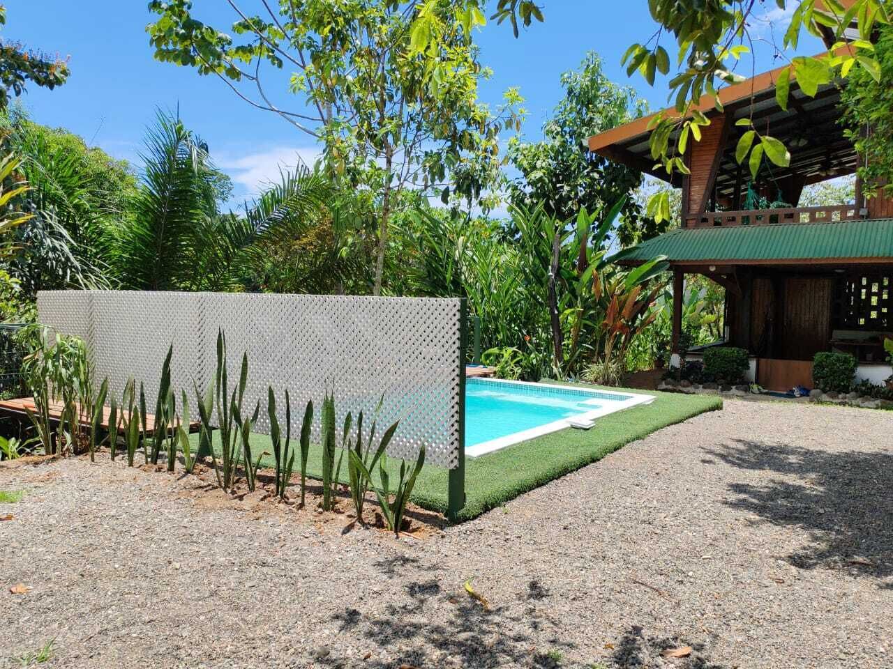 Un'area piscina con recinzione, una struttura in legno con tetto verde e vegetazione lussureggiante.