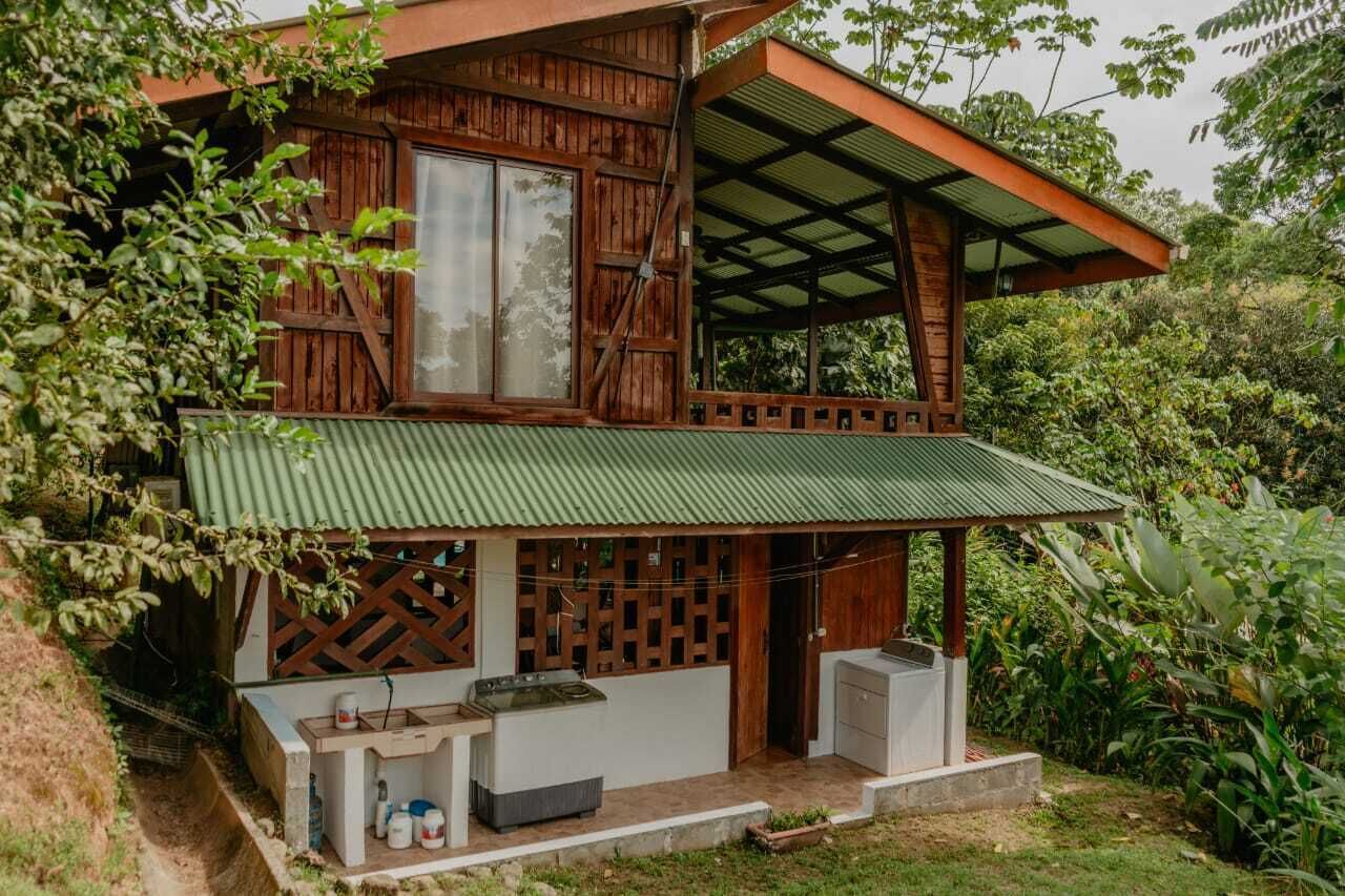 A rustic wooden house with a green metal roof, a covered porch, and a small outdoor kitchen area.