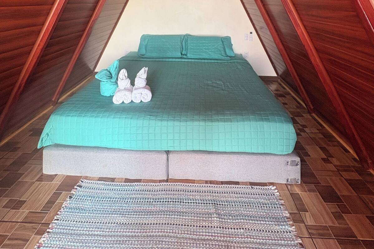 A narrow attic bedroom with a bed, a heater, and a hanging light fixture.