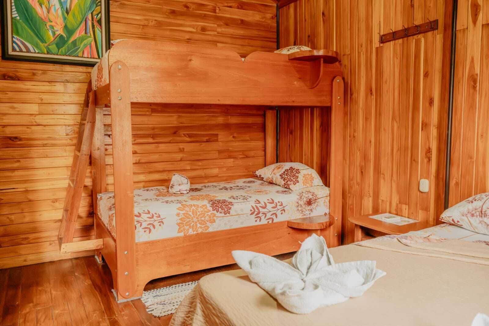A wooden cabin room with a bunk bed, a single bed, and a wooden ladder.